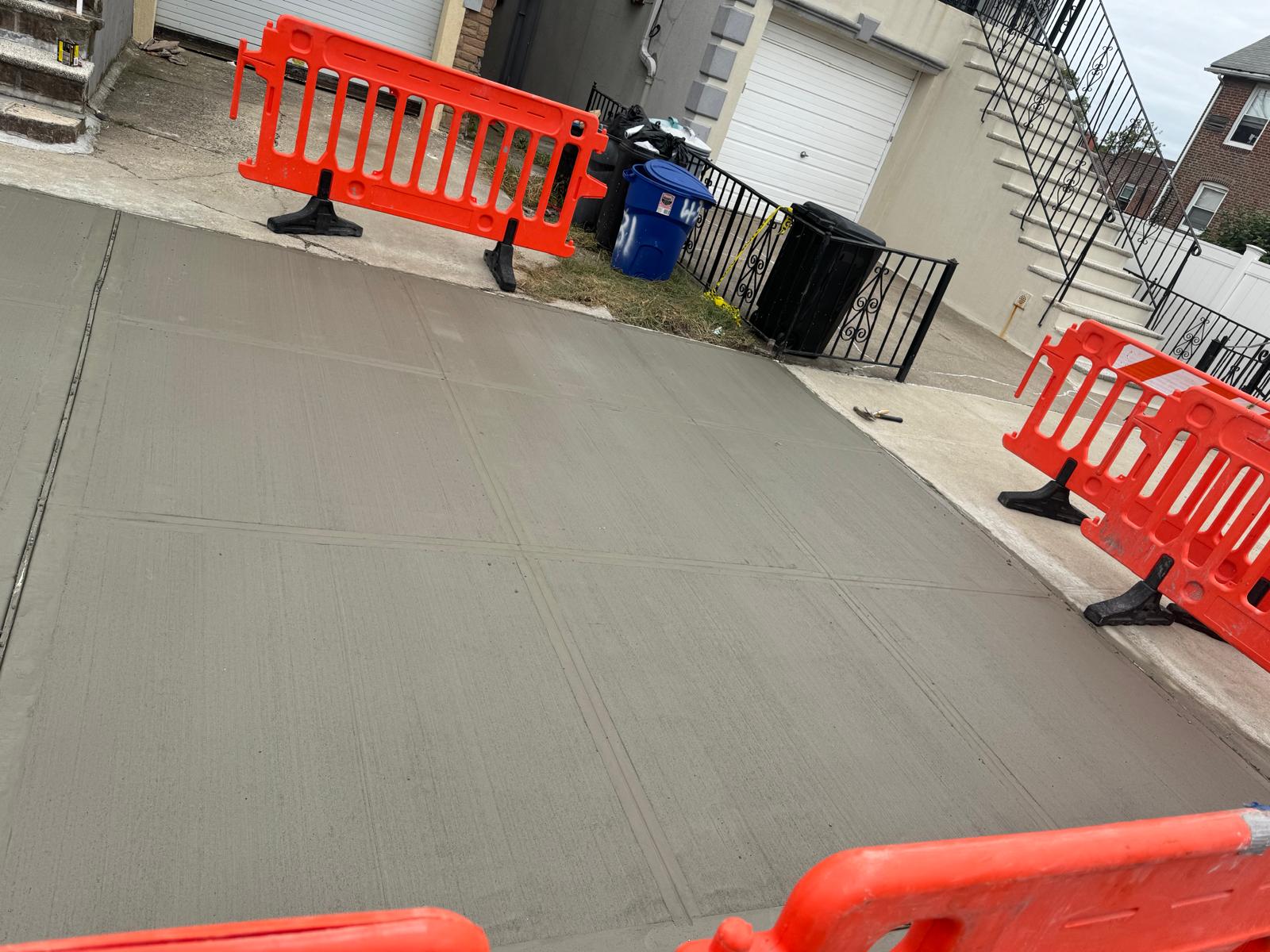 A concrete sidewalk lined with orange barriers, signifying an active concrete service project in progress.