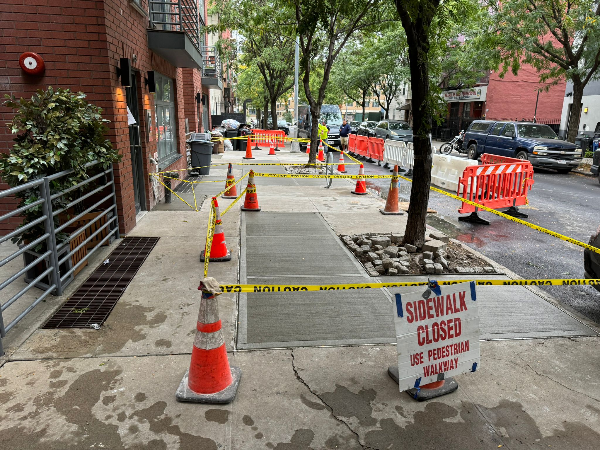 A street scene featuring construction cones and a closed sign, indicating sidewalk repair in progress.